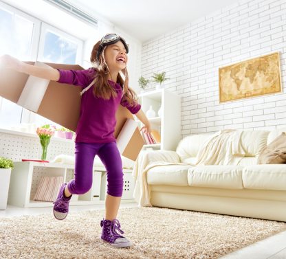 a young girl is carrying a box in a living room.