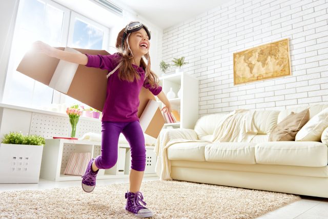 a young girl is carrying a box in a living room.
